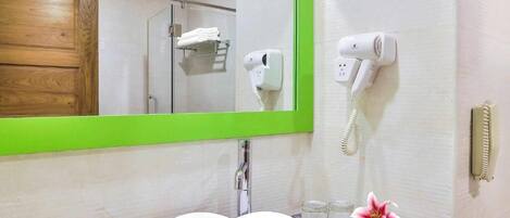 A bathroom with a heart-shaped sink, a green-framed mirror, a hairdryer, and a towel rack.