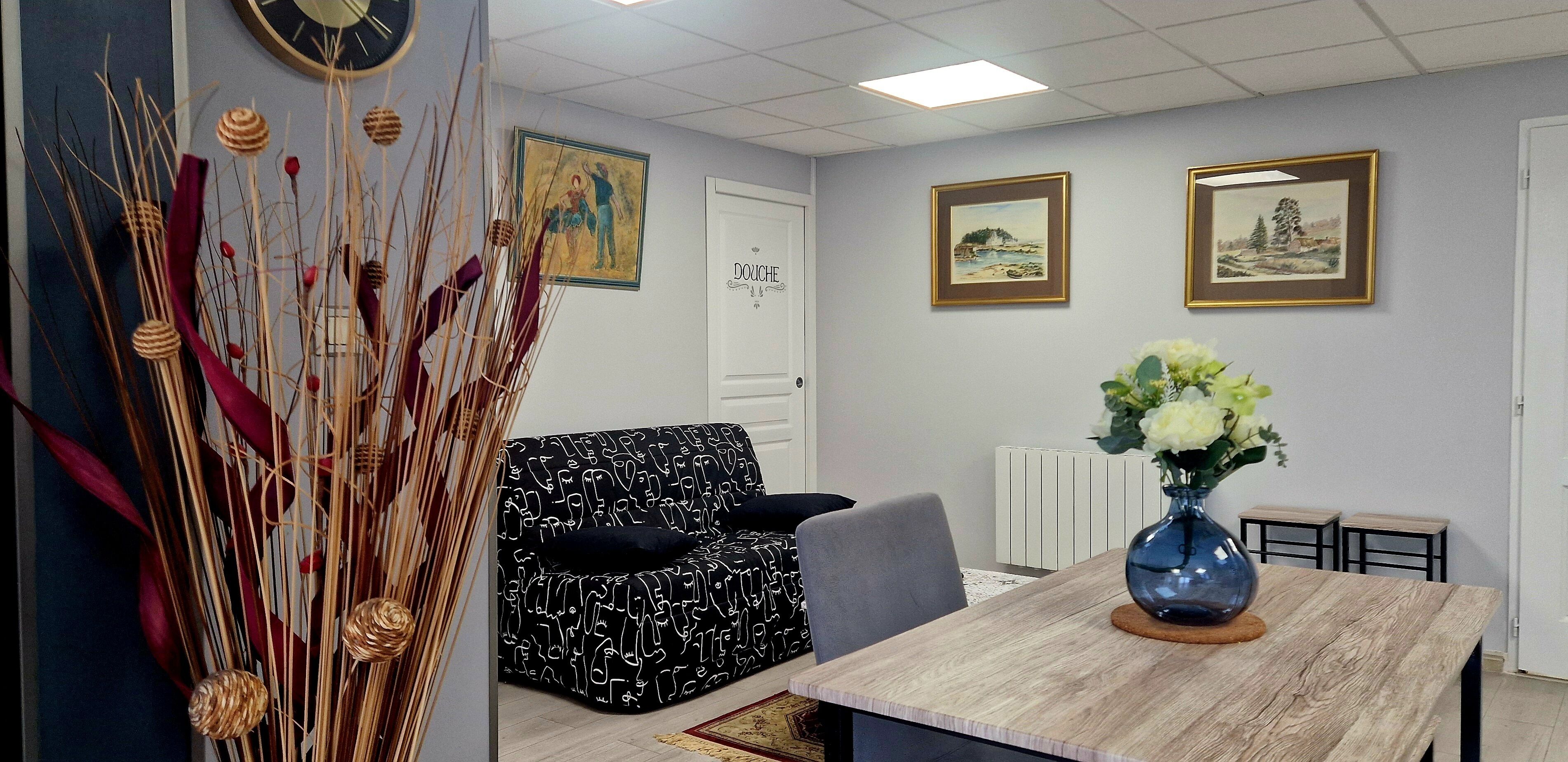 Ein Zimmer mit einem schwarz-weißen Sofas, einem Holzesstisch mit Blumenvase und zwei gerahmten Bildern an der Wand.