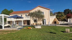Una casa a due piani con un portico coperto, un prato e un piccolo albero.
