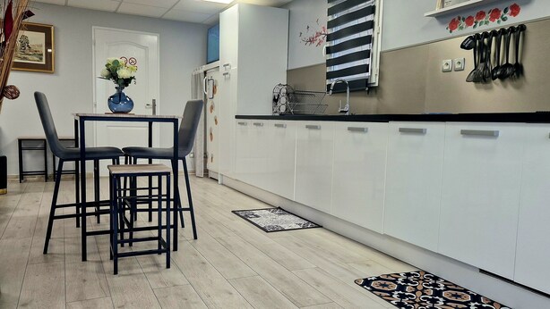 Una cucina moderna con mobili bianchi, un'area pranzo con tavolo e sedie, e uno schienale con utensili a portata di mano.