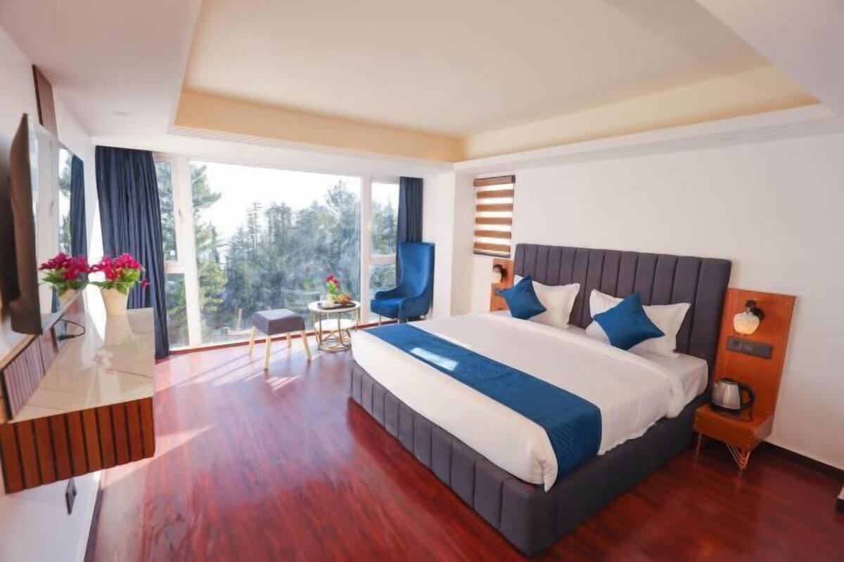 A modern hotel room with a large bed, a desk, a chair, a small table, and a view of the outdoors.