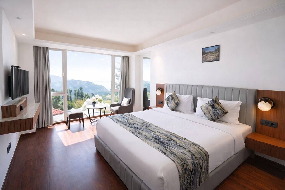 A modern hotel room with a large bed, a TV, a desk, and a balcony with a view of the mountains.