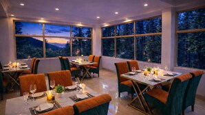 Ein Essbereich mit Tischen für zwei Personen, große Fenster mit Blick auf einen Wald und ein modernes Interieur.