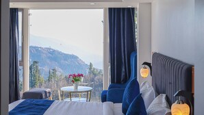 Ein Hotelzimmer mit einem großen Bett, einem Sessel, einem kleinen Tisch und Bergblick.