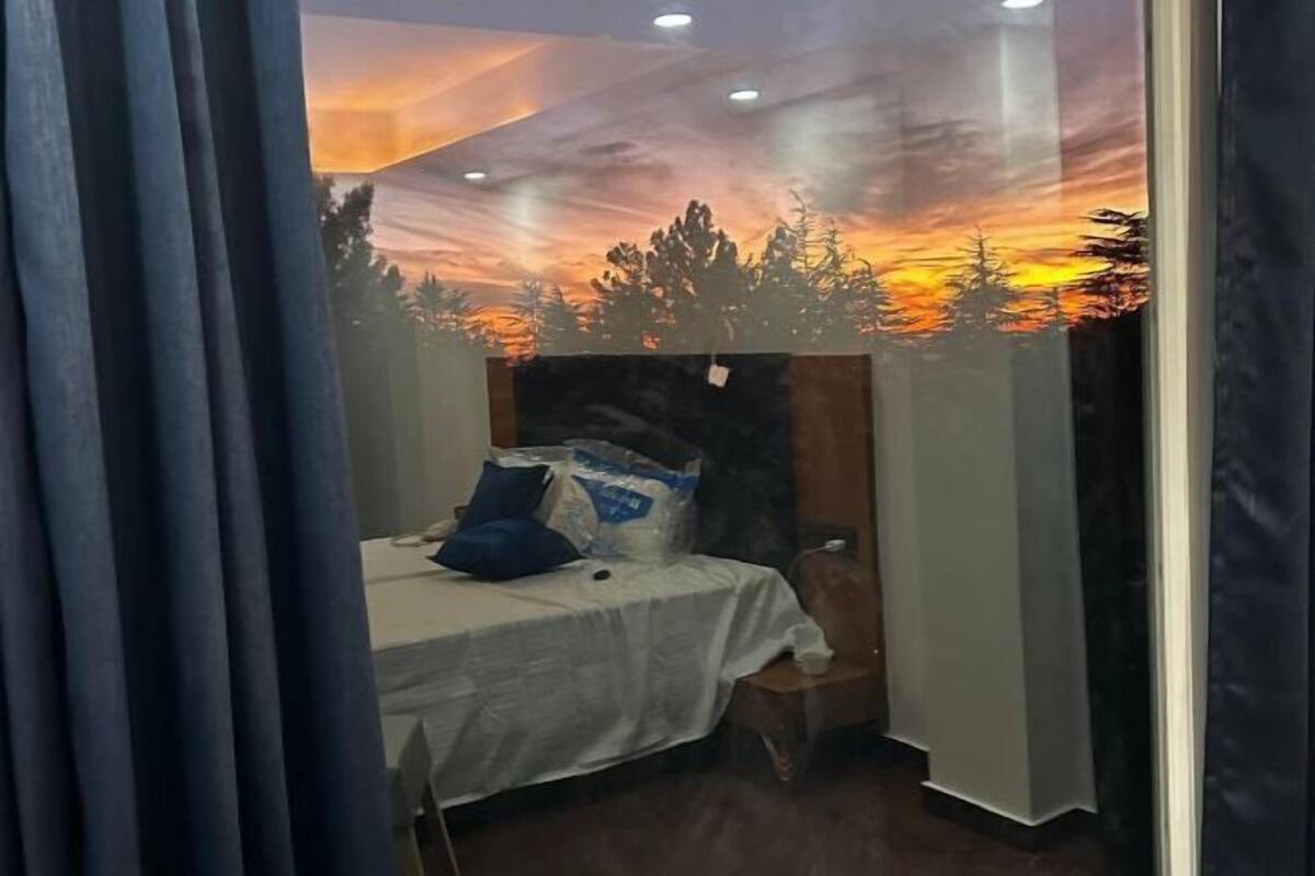 A bedroom with a bed, a nightstand, and a wall mural of a sunset.