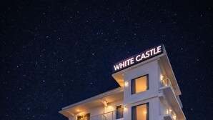 Ein mehrgeschossiges Hotel namens 'The White Castle' mit einem Stern-Logo, Balkonen und Blick auf den Nachthimmel.