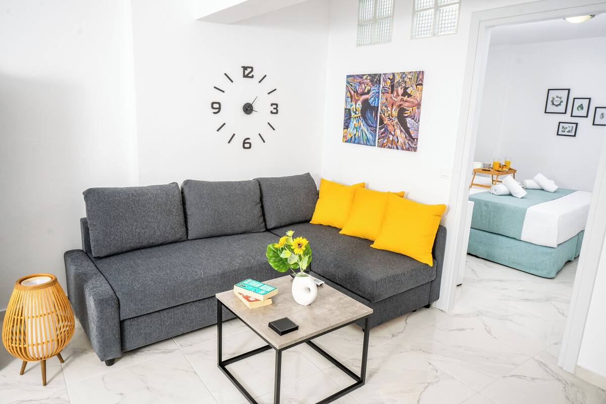 Uma sala de estar moderna com um sofá cinzento, uma mesa de centro, um relógio de parede e um quadro.