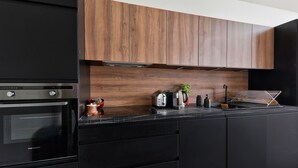 A modern kitchen with black cabinetry, a built-in oven, and a wooden backsplash.