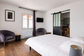 A bedroom with a bed, two chairs, a TV, a window with curtains, and a wardrobe.