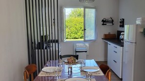 A dining area with a wooden table set for four, a black-framed window, and a kitchen area with a refrigerator and a sink. - House 400m from the beach, for 6 people (Penvénan)