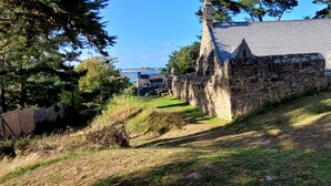 A stone building with a steep roof, surrounded by trees and a grassy area. - House 400m from the beach, for 6 people (Penvénan)