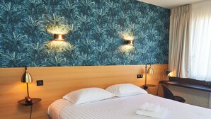 Una habitación de hotel con una cama, dos lámparas fijadas a la pared, un escritorio y una cortina.