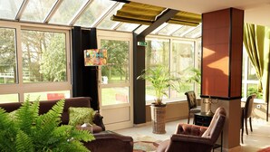 Una habitación soleada con ventanas amplias, un sofá de cuero marrón, una planta en maceta y un televisor sobre un mueble bajo.