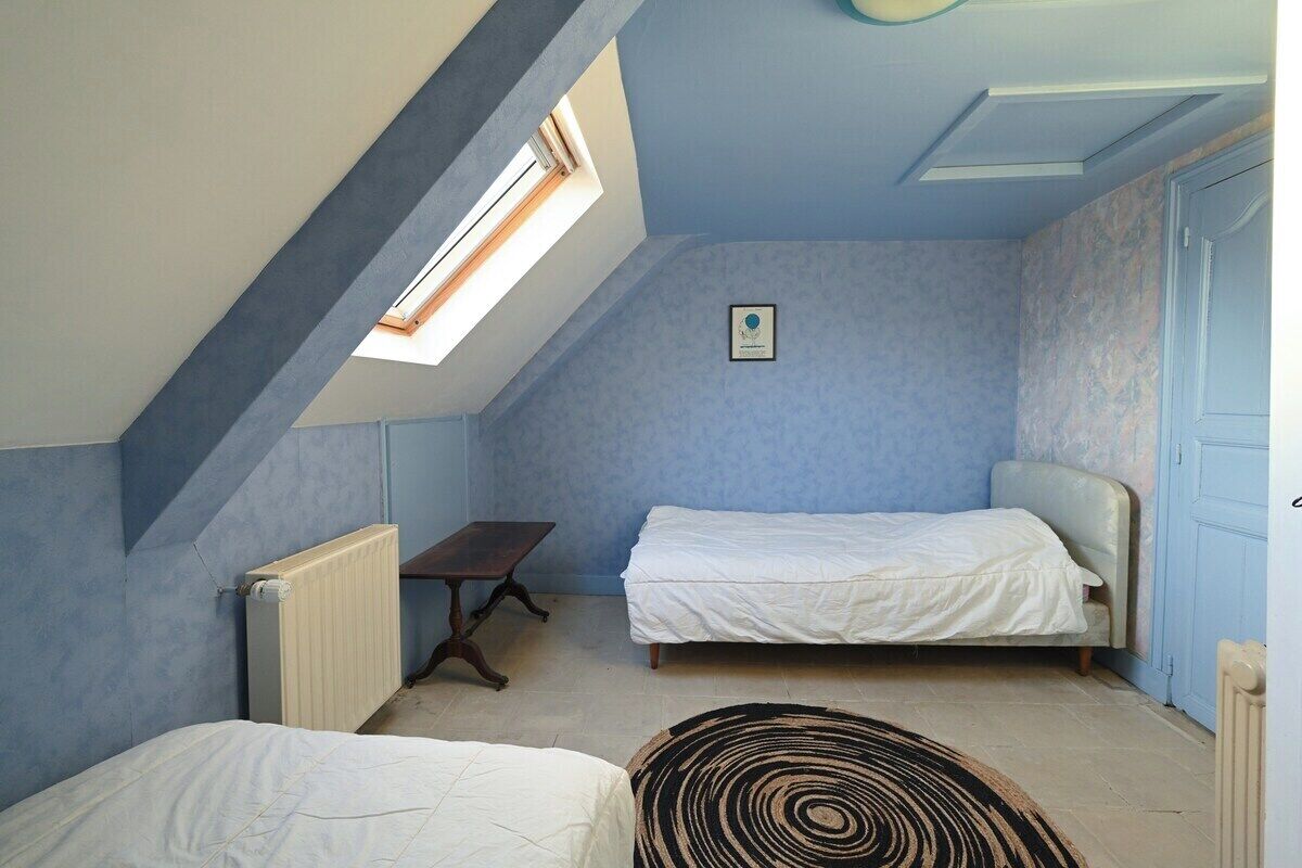 A small, single-room apartment with a sloped ceiling, a skylight, a bed, a small table, and a radiator.