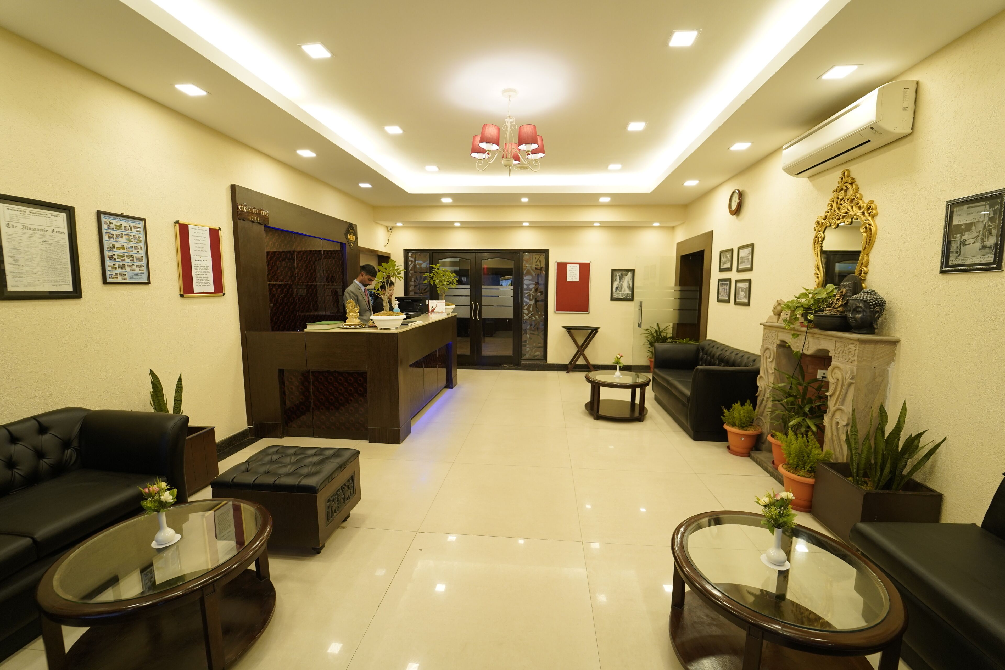 A hotel lobby with a reception desk, black leather sofas, a coffee table, and potted plants.
