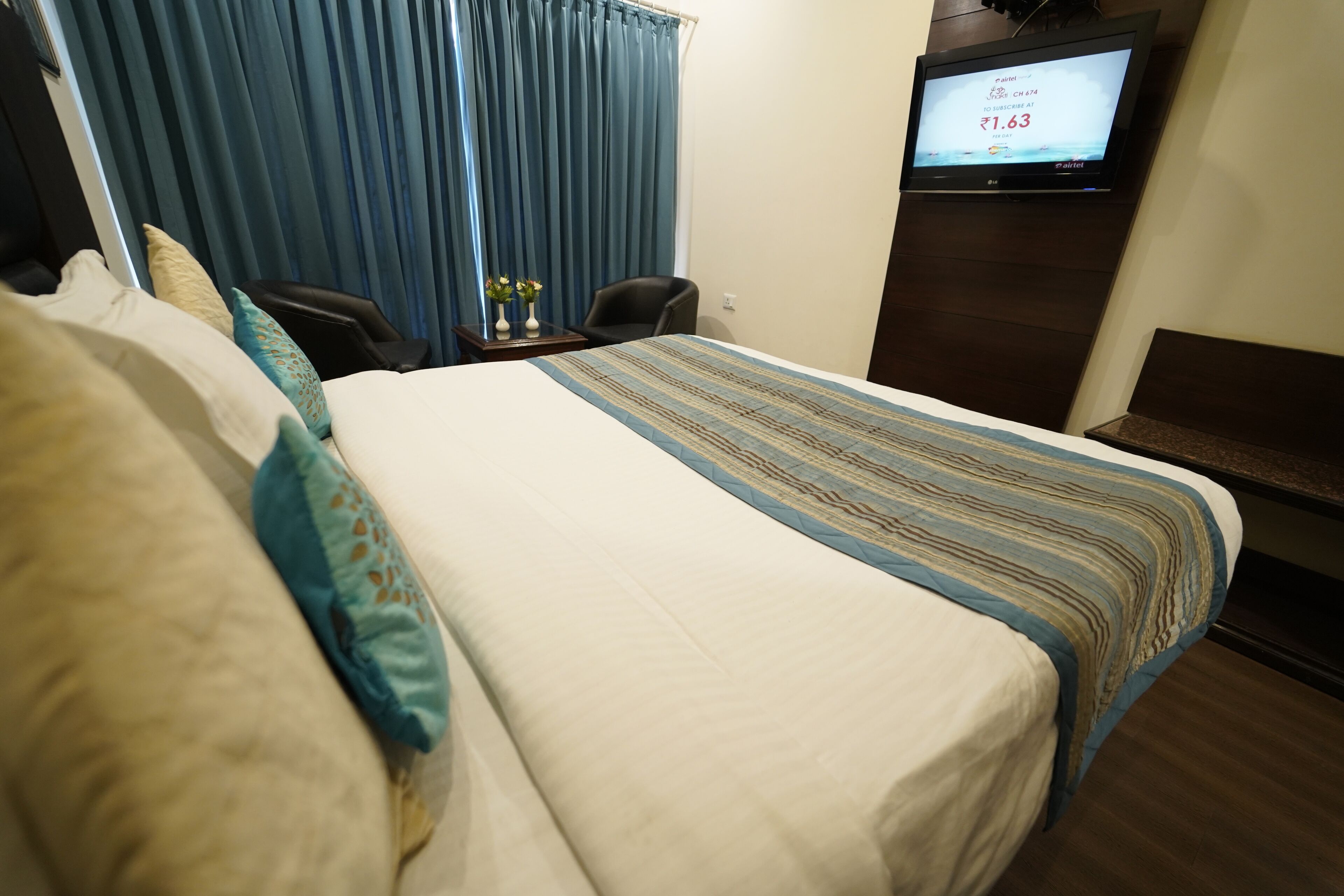 A hotel room with a large bed, a television on the wall, and a desk with a chair.