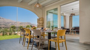 A dining area with a table set for four, a stone wall, and a view of the mountains. - Villa Hemèra, pool and relaxation a few minutes from Scopello (Sicilia)