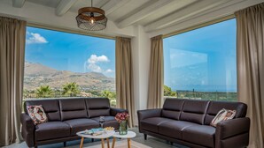 A room with two dark brown leather sofas, a small white table with a vase of flowers, and a view of a mountainous landscape through large windows. - Villa Hemèra, pool and relaxation a few minutes from Scopello (Sicilia)