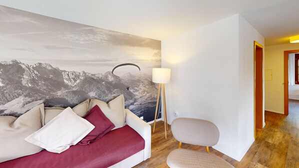 A room with a mountain mural, a sofa, a chair, and a floor lamp. - Reka-Ferienanlage Rougemont (Gstaad) (Rougemont)