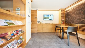A modern library with wooden bookshelves, a table with chairs, and a large wall mural. - Reka-Ferienanlage Rougemont (Gstaad) (Rougemont)