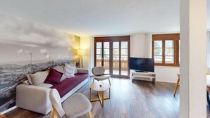 A living room with a sofa, a chair, a TV, and a mural of mountains. - Reka-Ferienanlage Rougemont (Gstaad) (Rougemont)