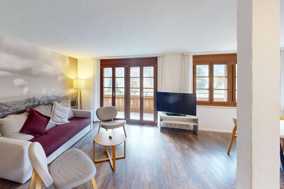 Ein Wohnzimmer mit einer Couch, einem Sessel, einem Fernseher und einer Bergwand.