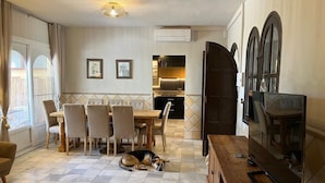 Ein Essbereich mit einem Holztisch und Stühlen, ein Hund liegt auf dem Boden und ein Fernseher steht auf einem Holzschrank.