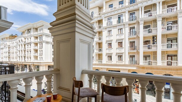 A balcony with two wooden chairs, a small round table, and a view of a multi-story building with balconies. - Boulevard 129 (Tashkent)