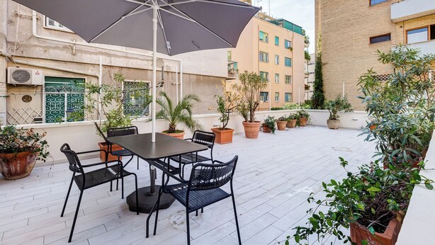A rooftop terrace with a table and chairs, surrounded by potted plants and a large umbrella. - Gianicolo Apartment with Terrace (Rome)