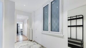 A hallway with white walls, a marble floor, a window with frosted glass, and a black metal rack. - Gianicolo Apartment with Terrace (Rome)