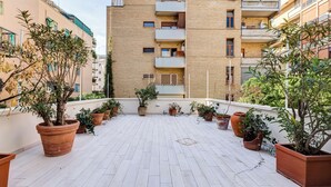 A rooftop terrace with terracotta planters and potted plants, surrounded by multi-story buildings. - Gianicolo Apartment with Terrace (Rome)