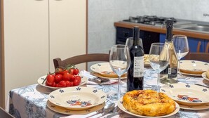 A dining table set with plates, glasses, and a bottle of wine, with a kitchen in the background. - On The Sea San Foca wifi Ac (Melendugno)