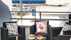 A balcony with wicker furniture, a table with food and drinks, and a view of a marina. - On The Sea San Foca wifi Ac (Melendugno)
