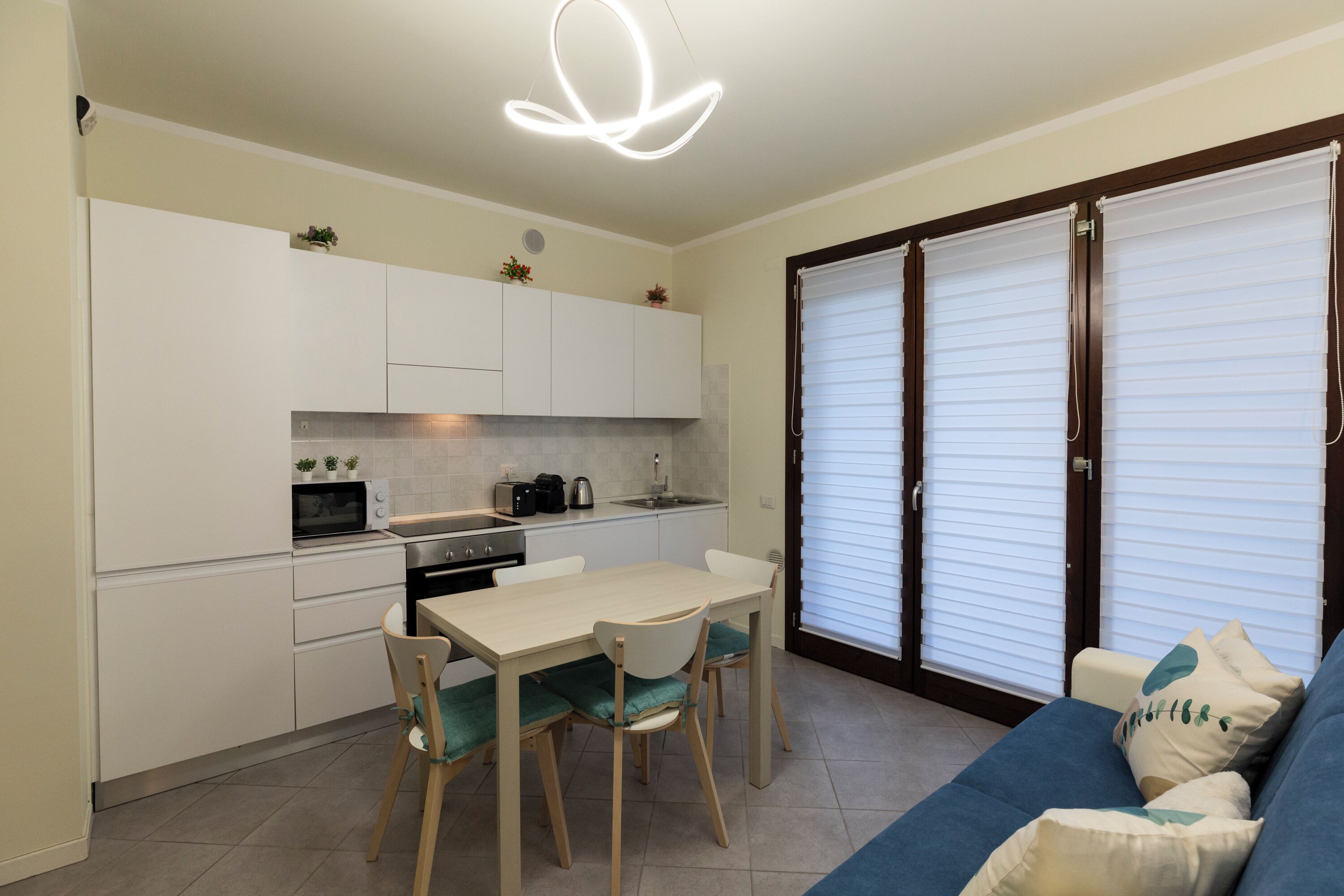 A compact kitchen with white cabinets, a dining table with chairs, and a blue sofa with cushions.