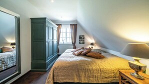 A bedroom with a large bed, a wardrobe, a window with curtains, and a lamp on a bedside table.