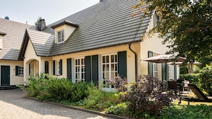 A traditional European-style building with a tiled roof, green shutters, and a paved courtyard.