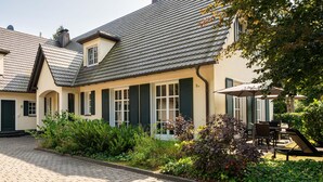 Een traditioneel Europees gebouw met een pannendak, groene luiken en een geplaveid binnenterrein.