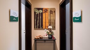 Een hal met twee deuren, elk met een bordje met de naam 'Lindemuth'. In het midden staat een zwarte console tafel met een bloemenvaas en een decoratieve schaal.