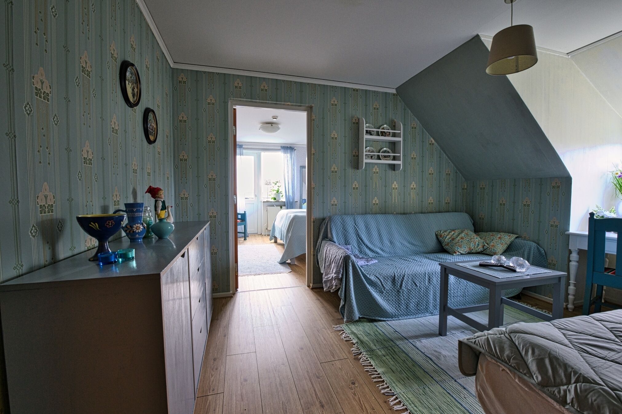 A cozy room with a sloped ceiling, a sofa, a table, and a kitchen area with a counter and cabinets.