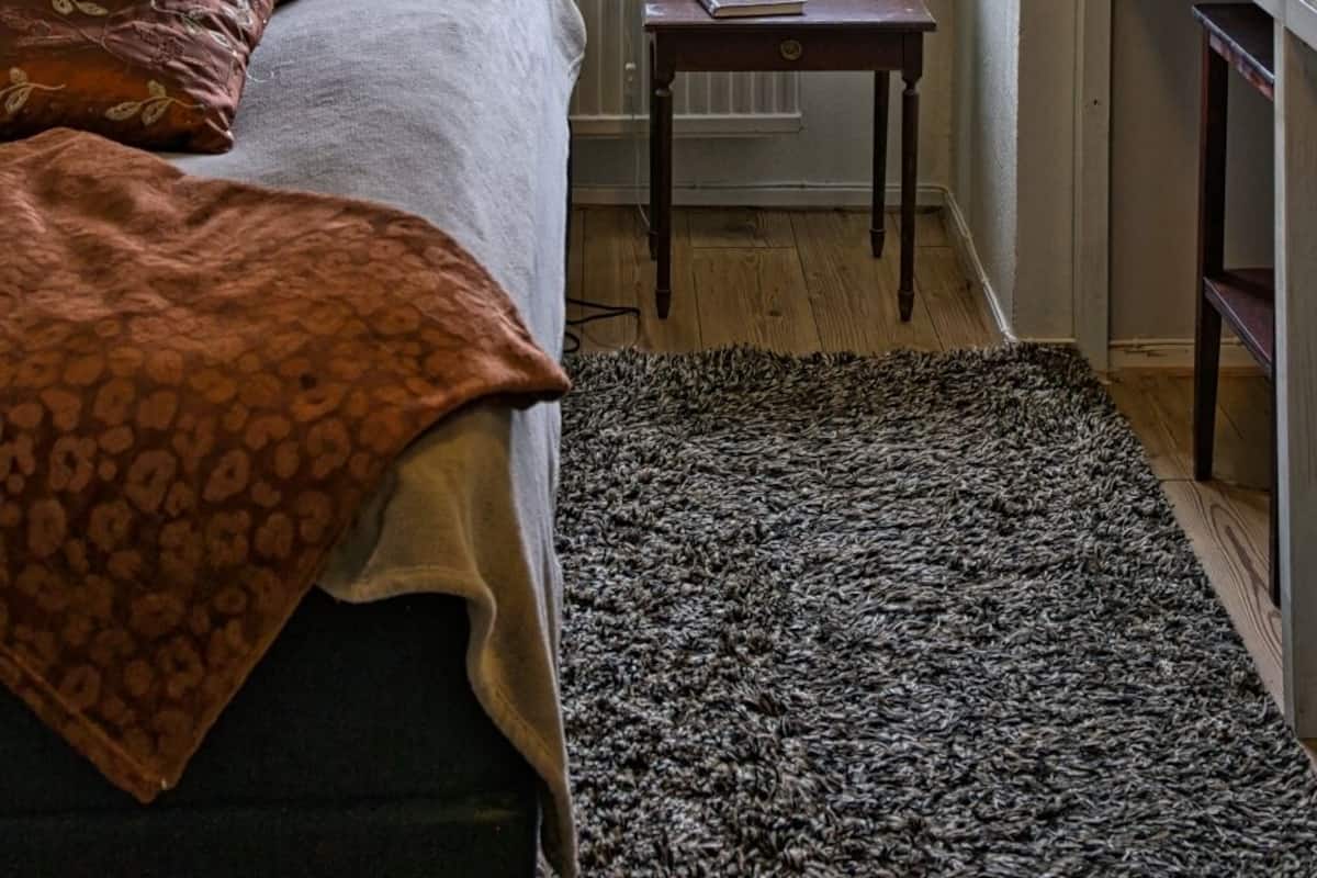 A bedroom with a bed, a radiator, a window with curtains, a desk, and a plant.