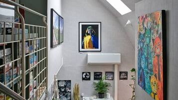 Una escalera con barandilla de metal, una estantería, una silla roja y un cuadro en la pared.