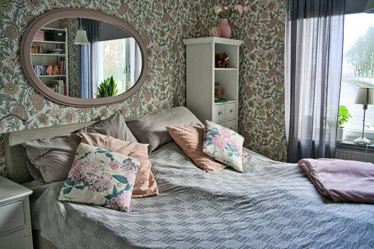 A bedroom with a bed, pillows, a nightstand, a dresser, a mirror, and a window with curtains.