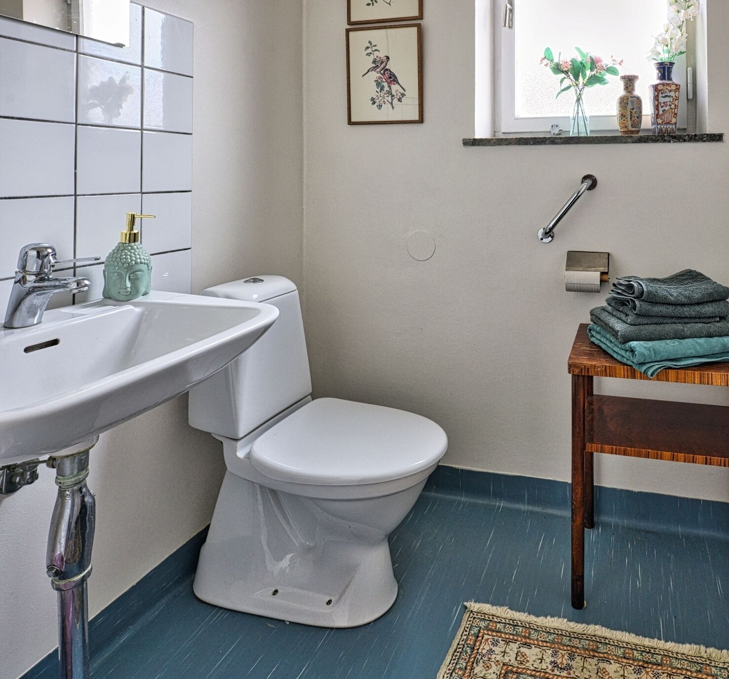 Ein Badezimmer mit Toilette, Waschbecken, einer grünen Flasche und einem Fenster mit Blumen.