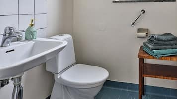 Un bany amb un vàter blanc, un lavabo amb una ampolla verda i una finestra amb flors.