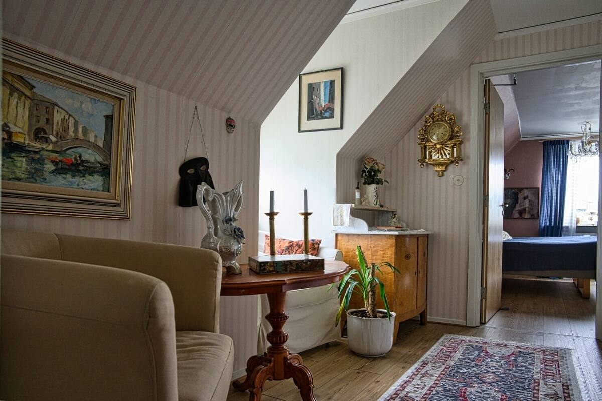 A cozy living room with a sofa, a wooden side table, a potted plant, and a painting on the wall.