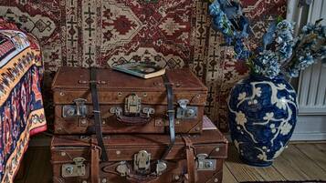 A stack of brown leather suitcases with metal clasps, a book, and a blue and white vase with flowers on a wooden floor.