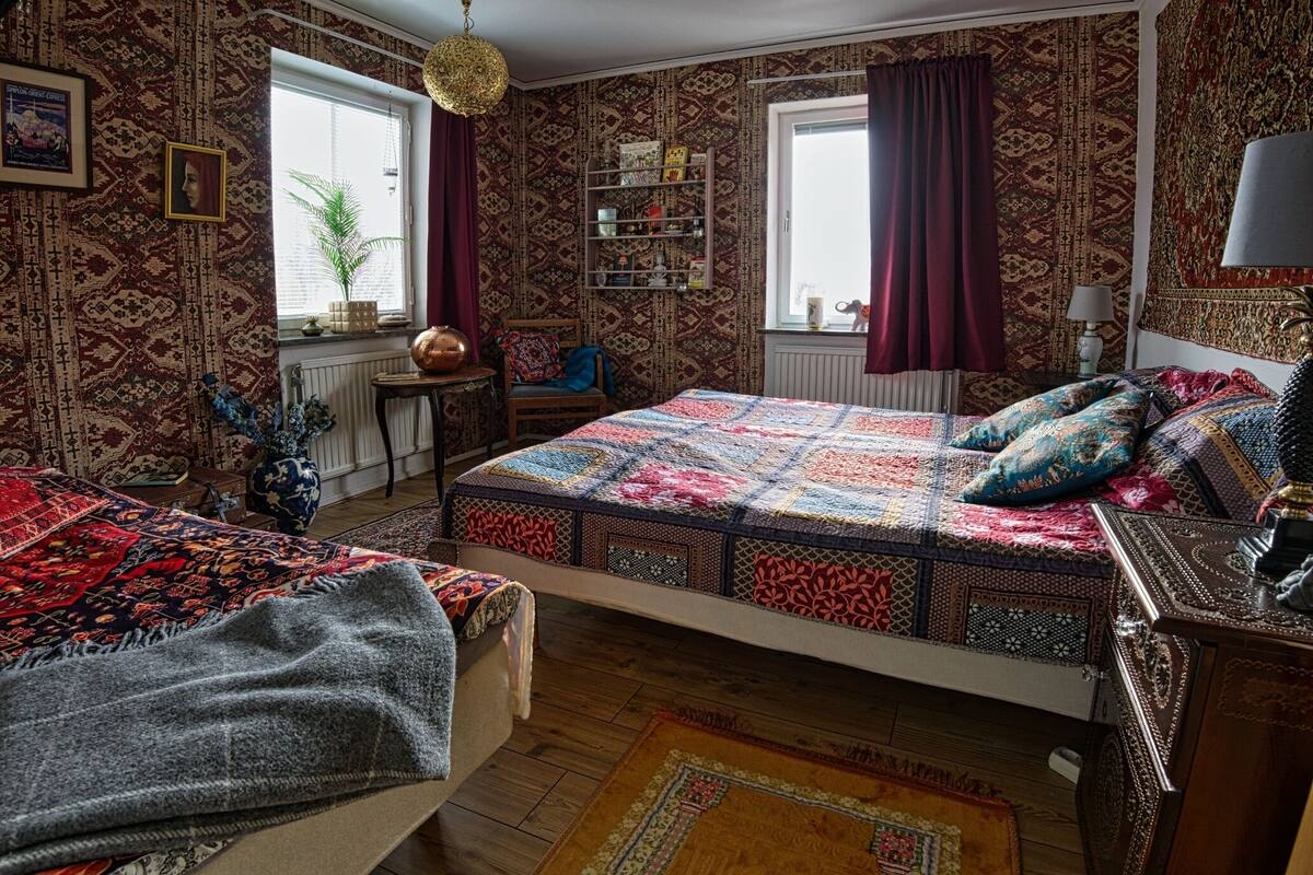 A traditional room with a large bed, a small table, a chair, a bookshelf, and a window with curtains.