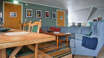 A cozy living room with a wooden dining table, a blue sofa, and a colorful striped rug.