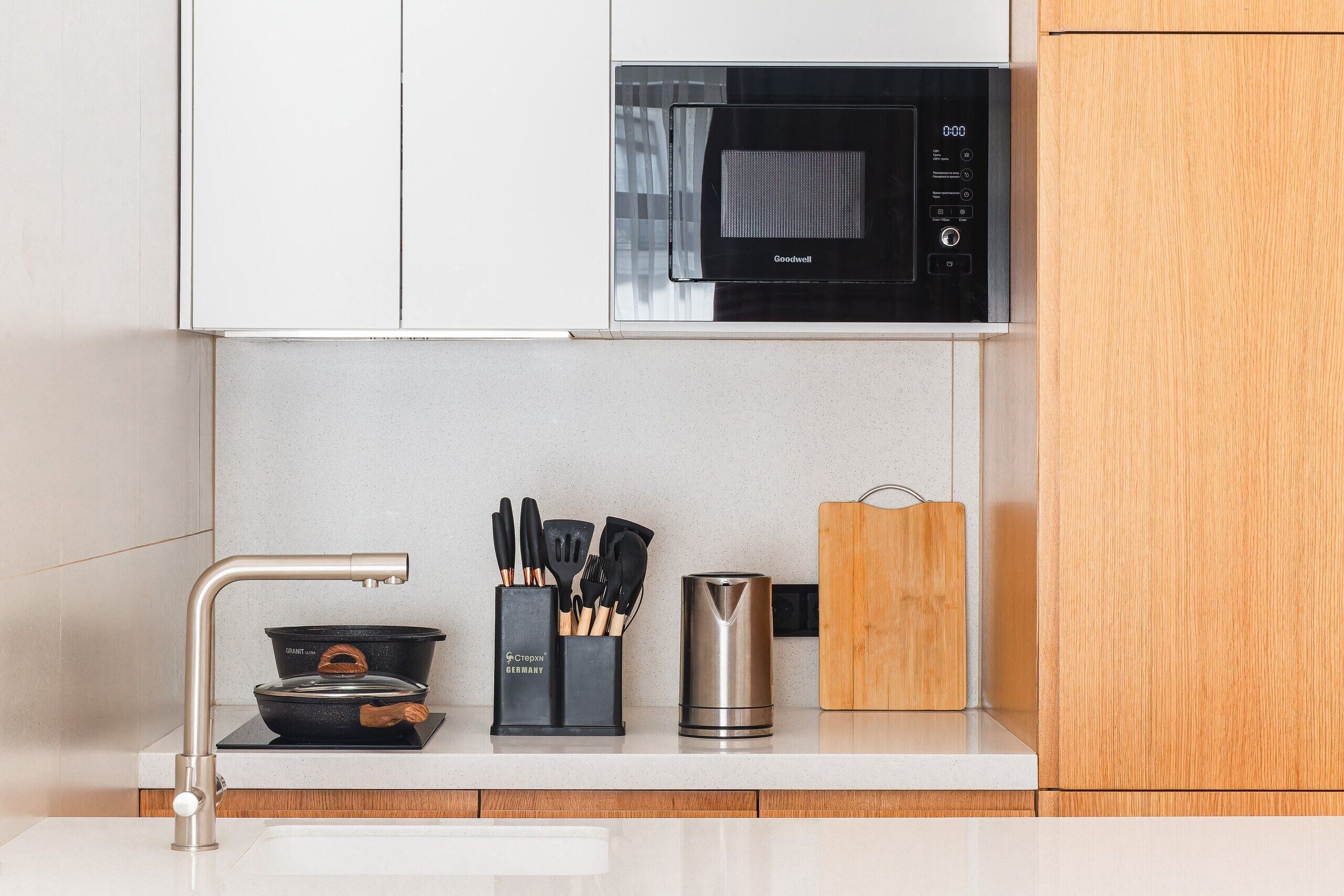 A modern kitchen with a built-in microwave, a stainless steel kettle, and a pot set on an induction cooktop.