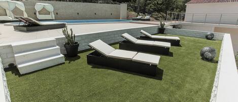 Un área junto a la piscina con sillones de descanso, una piscina pequeña y un muro de piedra.